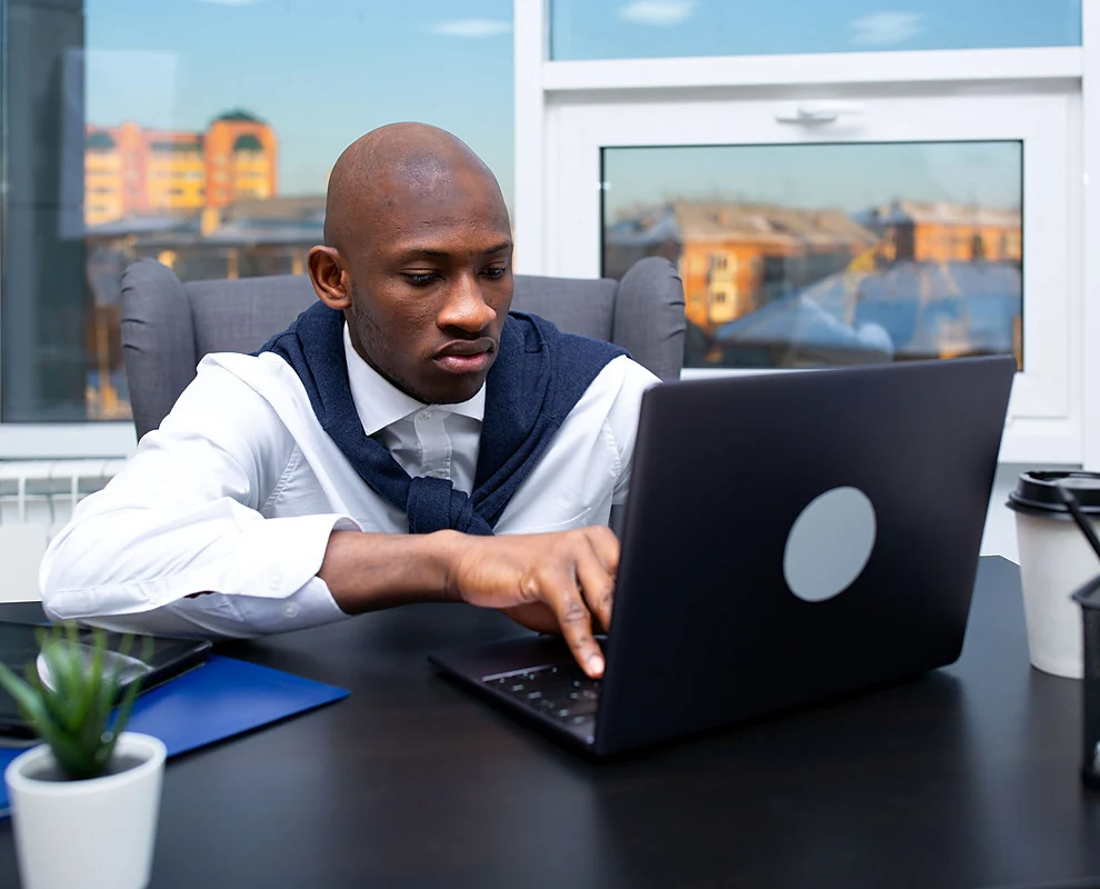 A business owner working on a laptop in an office with a city view